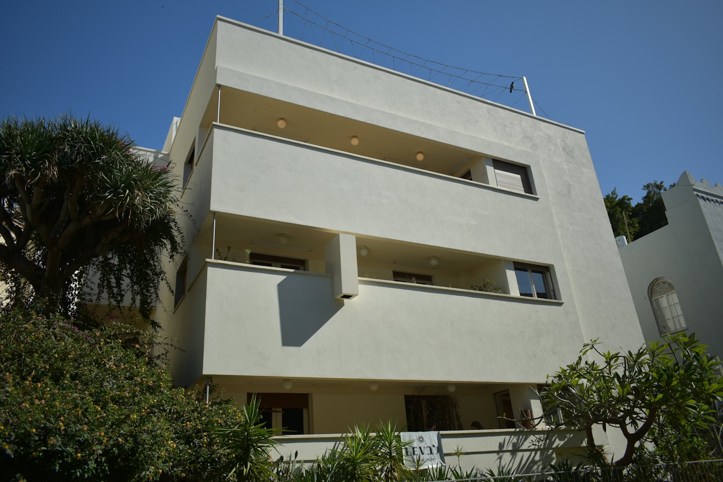 Edificio de apartamentos modernista con balcones escalonados y vegetación exuberante.