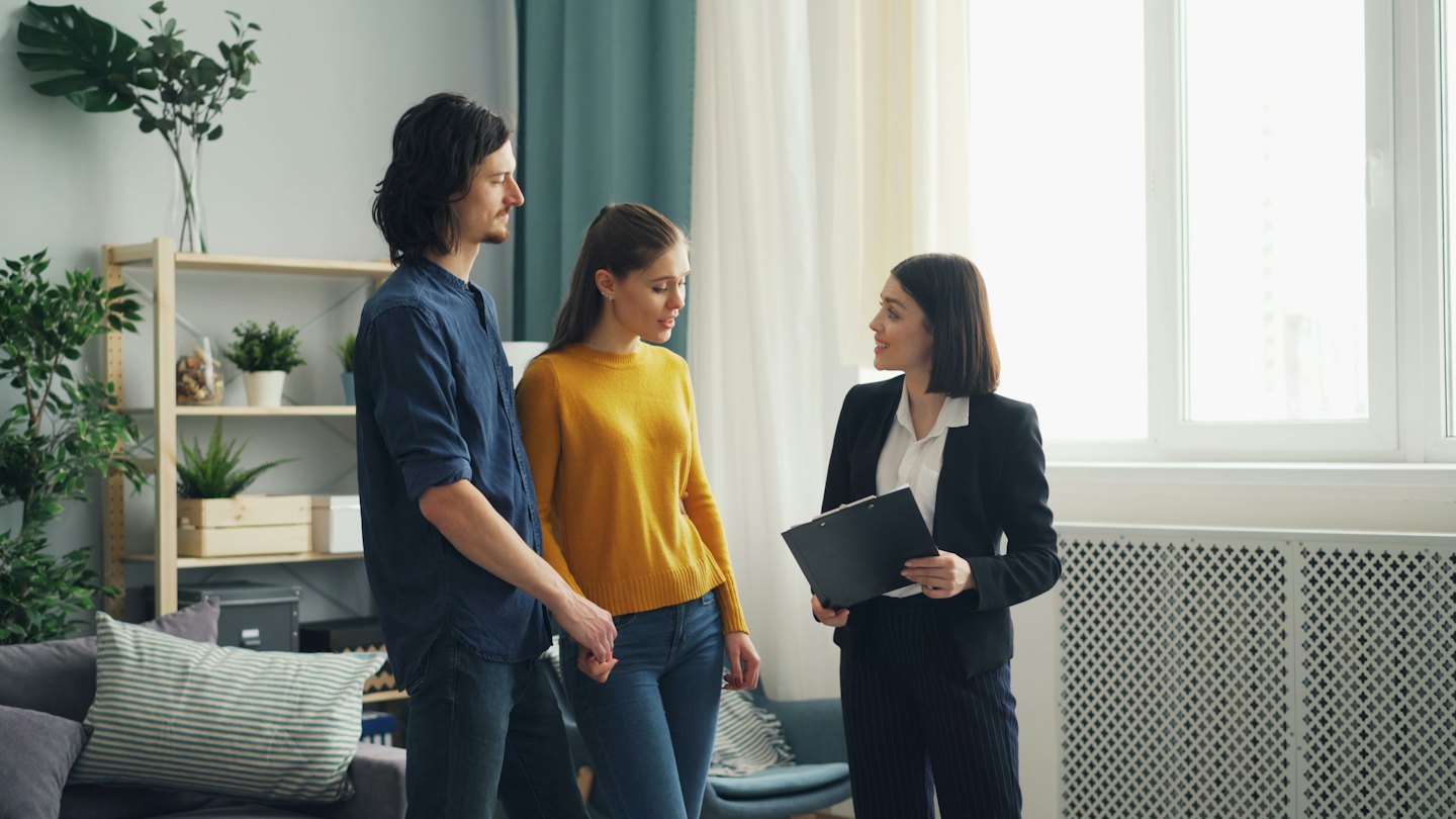 Agente inmobiliario muestra plano de apartamento a una pareja.